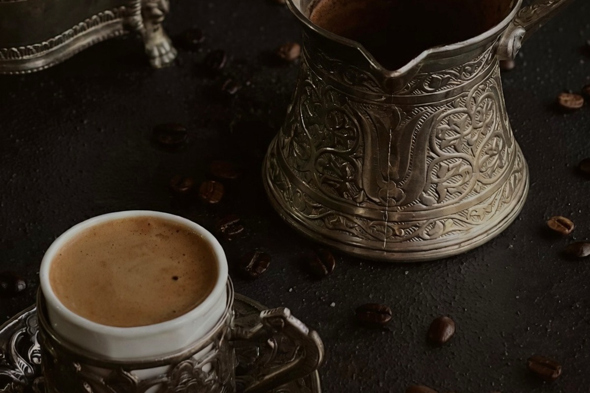 Turkish coffee being poured from a cezve into a patterned cup