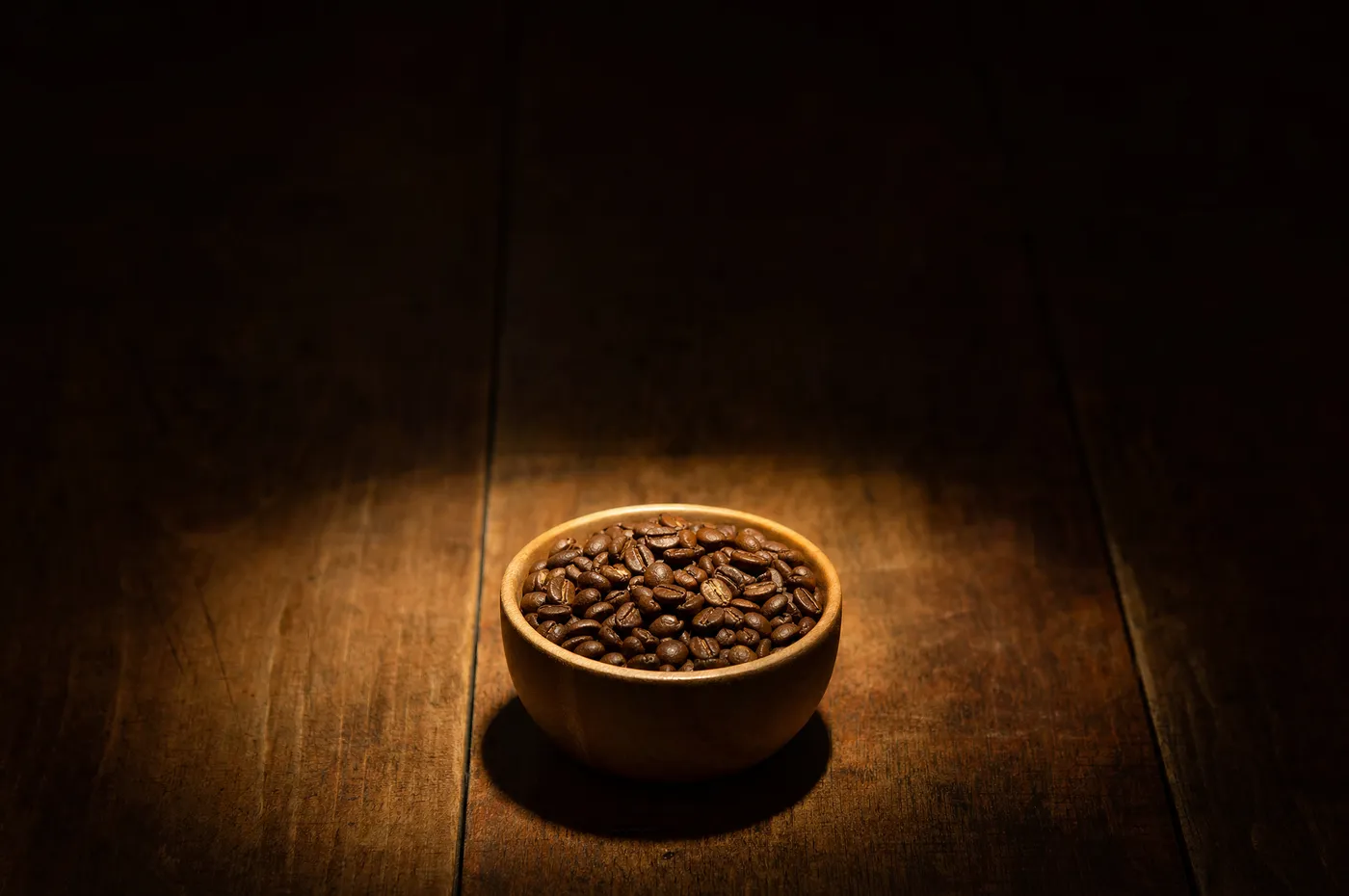 A single bowl of roasted coffee beans alone in a pool of light