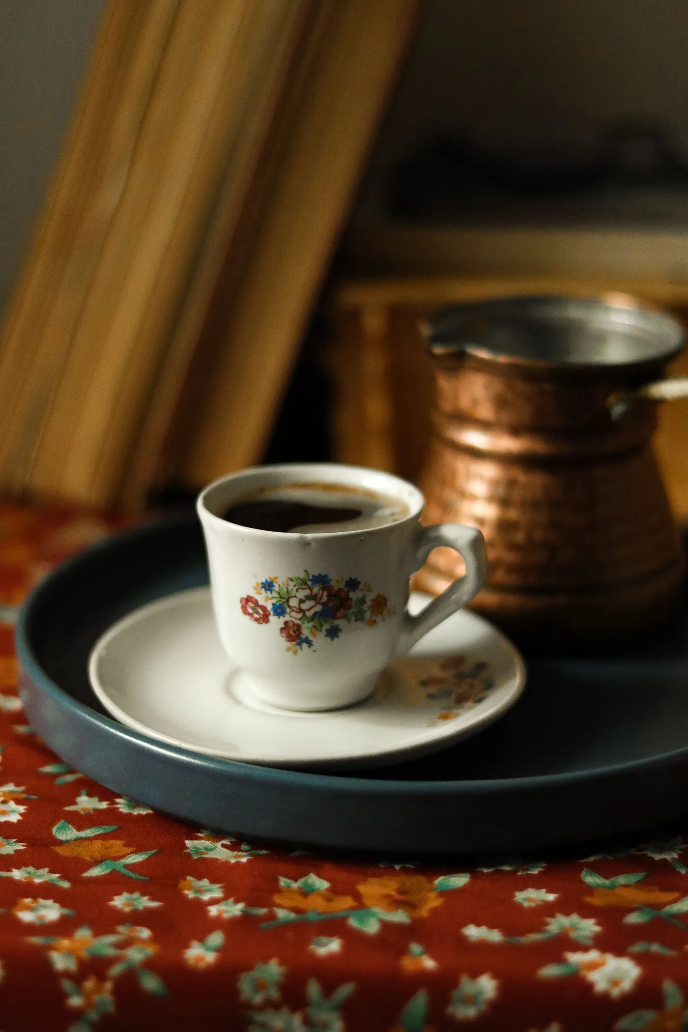 A cup of Turkish coffee beside a copper pot on a patterned rug